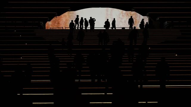 Dramatic wide perspective showing anonymous city people walking upward into a giant illuminated orange portal arch.