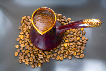Artistic shot of a cezve with rich Turkish coffee on a gray surface, accented by roasted beans....