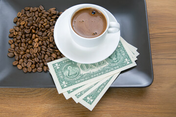 Hot espresso in a white ceramic cup placed on a saucer, next to scattered coffee beans and a stack...