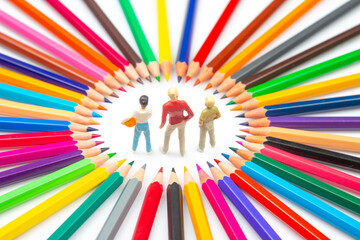 A creative composition featuring three small figures within a circle of assorted colored pencils,...