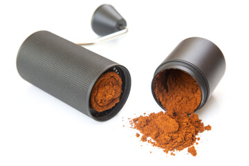 Disassembled black coffee grinder with a metallic handle displays finely ground coffee, spilling...