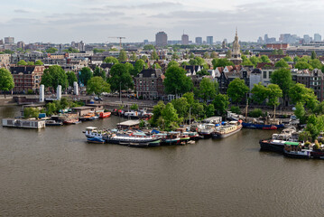 An expansive aerial view of an Amsterdam canal or river, dotted with boats and flanked by tree-lined banks and distant city buildings