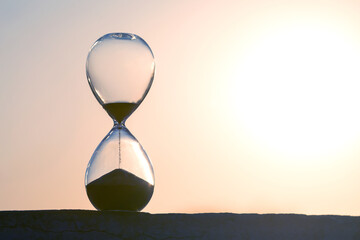 Hourglass framed by a radiant sunset, sand trickling down in soft light. Great for illustrating...