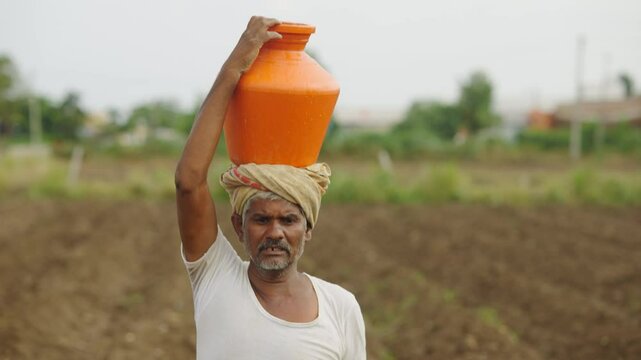 The Indian farmer is walking with a pitcher on his head in the agricultural field