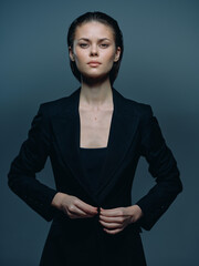 serious woman in black blazer adjusting jacket with focused expression against dark gray background...