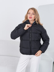 Fashionable woman model poses in stylish black puffer jacket in modern studio setting