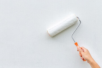 Hand painting white wall with paint roller, close-up shot showing DIY home improvement or renovation.