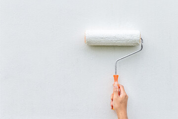 Obraz premium Hand painting white wall with paint roller, close-up shot showing DIY home improvement or renovation.