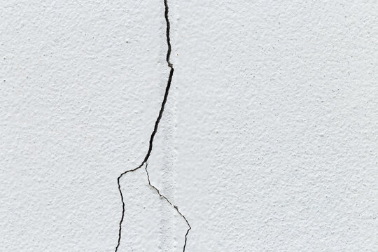 White wall surface with long vertical cracks, symbolizing structural damage, aging, or poor construction.