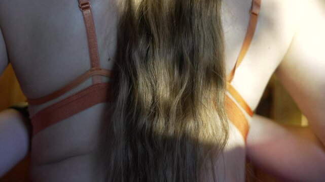 Back Hair Bra Closeup of woman with long hair adjusting orange bra strap indoors