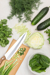 Spinach leaves in white bowl. Green onions and knife on cutting board.