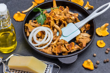 Fried chanterelle mushrooms, spatula and chopped onion in pan. Raw chanterelles on table
