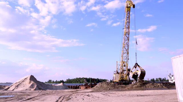 Yellow industrial crane with a grab bucket. Extraction of river sand.