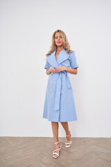 Blonde woman posing in a stylish studio wearing a light blue dress with elegant detail