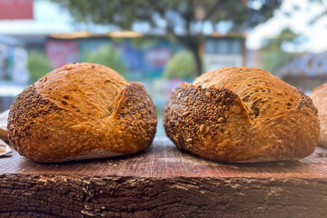 Close-up of two freshly baked, glossy breads topped with seeds, resting on a rustic wooden surface...