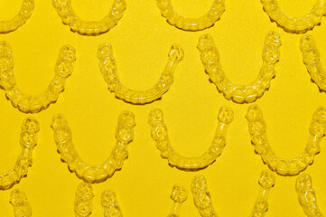 Clear dental aligners on colored yellow background, close-up side view from above. Pattern of clear...