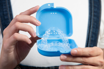 Woman holding clear retainers with box in hands, front view on background of girl's body in...