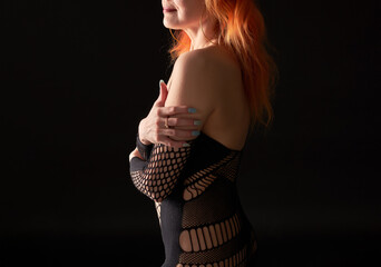 A woman with red hair and orange streaks in her hair is dressed in a black outfit with mesh...
