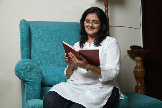  Indian woman reading book. Cheerful spending time indoors with captivating story. Hobbies and pastimes concept - Powered by Adobe