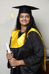 Half shot of Indian young graduate girl in graduation gown and cap.