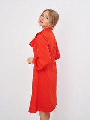 Woman in bright red knee-length dress with long sleeves, standing on wooden floor. Her hair is...