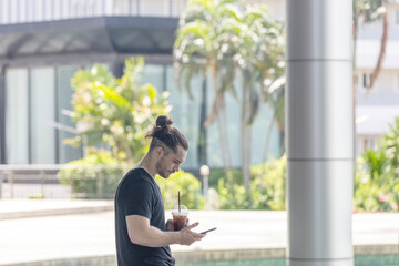Fototapeta premium An attractive fitness male trainer is taking a refreshment drink and checking his online exercise application on smartphone, Young and handsome man with technology