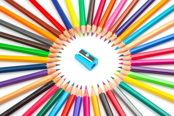 A vibrant circle of colored pencils surrounding a blue pencil sharpener on a white background....