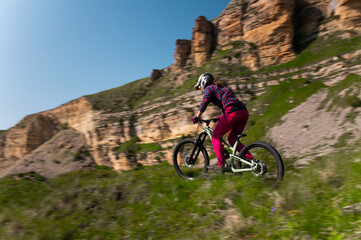Downhill mountain bike rider against epic cliffs on sunny day. Motion blur of mountain biker high...