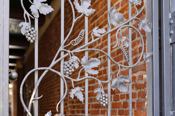 Artistic metal gate with grapevine motif and leaves, set in front of an old red brick wall.
