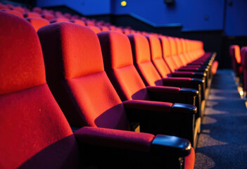 Row of red theater seats illuminated by colorful stage lighting in an auditorium