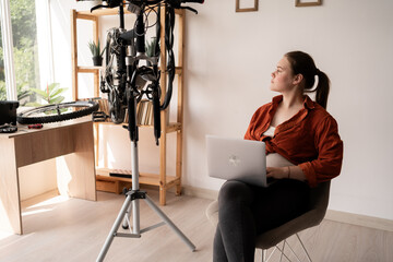 Young woman in casual clothes with laptop repairing bicycle at home