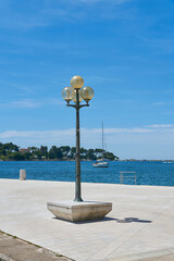 Laterne auf der Uferpromenade im Hafen von Porec in Kroatien. Im Hintergrund die Insel Sveti Nikola.