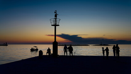 Silhouette von Menschen am Ufer der kroatischen Hafenstadt Porec in der blauen Stunde nach Sonnenuntergang