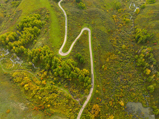 A top-down aerial view highlights a winding road snaking through hills and forests adorned with vibrant autumn foliage