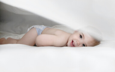 Adorable Baby Smiling Under Soft White Covers in Bright Natural Light