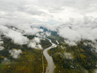An aerial perspective reveals a river winding through vast autumn forests, with low-lying clouds...