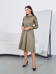Brunette model showcasing elegant olive green dress in modern studio setting