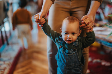 A parent guiding a young toddler while walking indoors, portraying early childhood moments,...