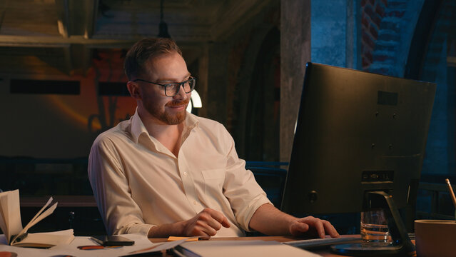 Caucasian man business guy businessman male workaholic in dark night office late time working typing computer smiling satisfied finish online work complete accomplishment internet task happy job done