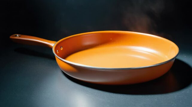 A bright orange frying pan placed on a dark surface, ideal for use in still life photography or as a prop in cooking scenes