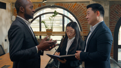 African American man businessman talking with Korean Asian guy male colleagues two men multiracial businessmen teamwork collaboration Japanese Chinese woman businesswoman secretary check documents