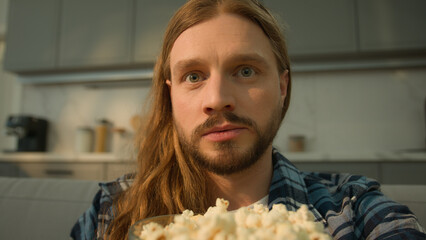 Focused concentrated Caucasian man guy male eating tasty corn popcorn eat overeating obesity watching TV watch television online program series film movie at home weekend relaxing enjoying close up