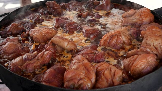 Traditional braised pork knuckles (Schweinshaxe) simmering in a large cauldron at an outdoor food festival or market.Close-up of savory pork shanks being slow-cooked in a rich sauce