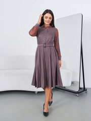 Fashion woman model poses elegantly in studio wearing stylish dress and heels