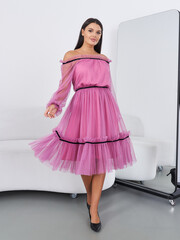 Brunette woman modeling stylish pink dress in modern studio setting