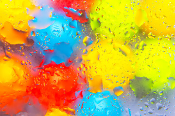 Colorful water droplets in red, yellow, blue, and green tones on a shiny surface, offering a bold...