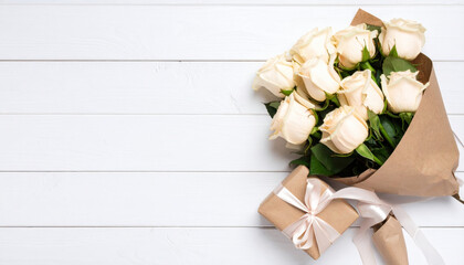 Bouquet of white roses wrapped in kraft paper with gift box on white wooden background