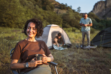mature woman hold cup and enjoys camping with her family