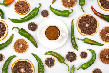 A white cup of cappuccino with foam, surrounded by dried orange slices and green chili peppers on a white background, creating a vibrant and spicy aesthetic.