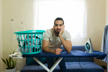 Bored man leaning on ironing board with basket full of clothes